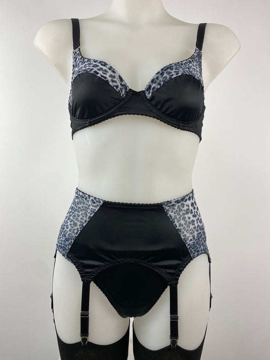 The Pip & Pantalaimon Monochrome Underwired Bra with black satin lower cups, sheer leopard mesh top cups, vintage-style projection, and dual fastening, shown from the front.