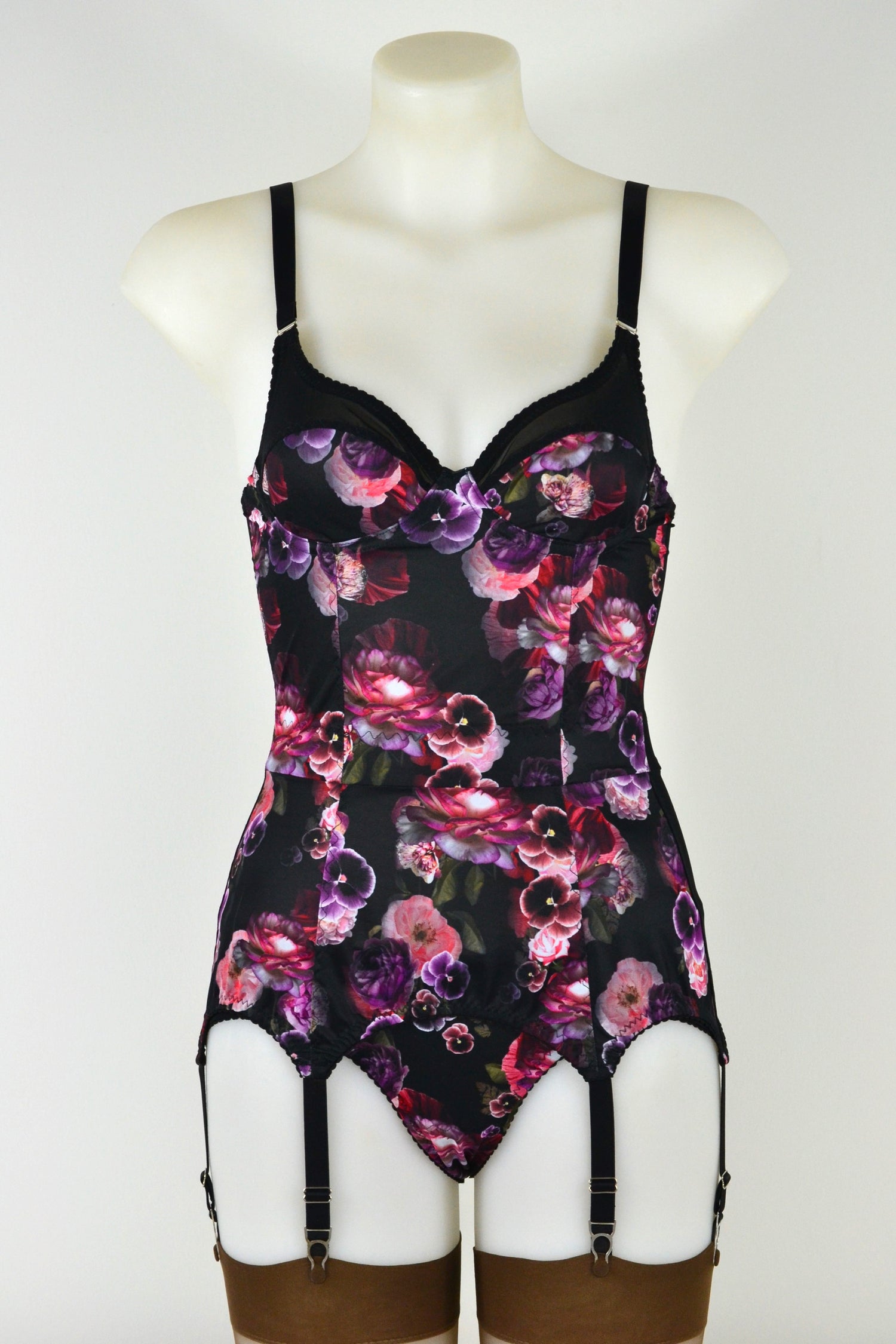 Black lingerie corselette with colourful floral pattern on a mannequin against a white background. custom vintage inspired shapewear made to order, including six suspender straps with metal garter clips