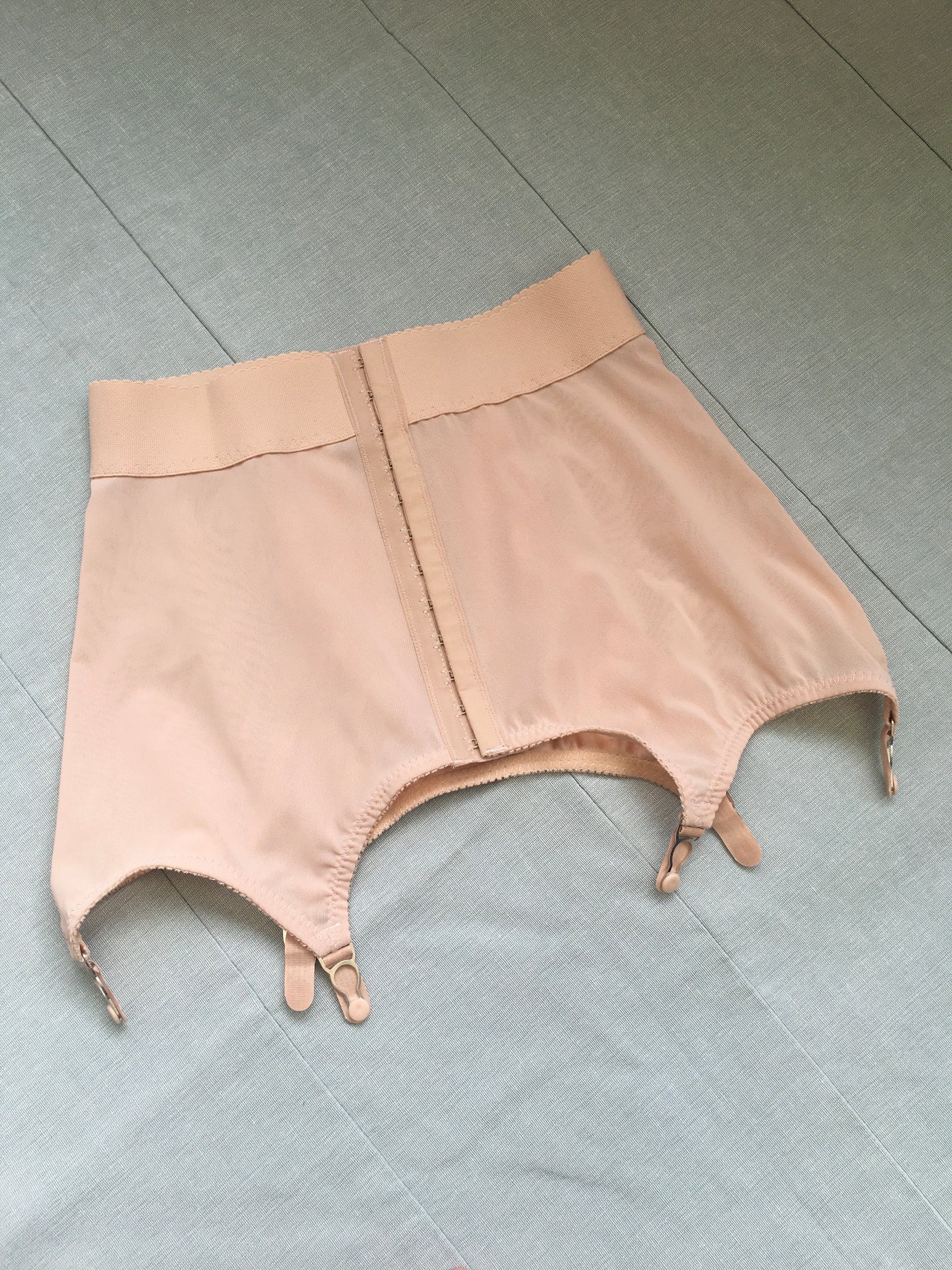 Vintage 1950s inspired shapewear lingerie underwear girdle girdlette longline 1940s suspender belt garter belt in muted vintage peach biscotti colour. Embodded large polka dot Goodwood pattern. Nude 1940s lingerie with six steel suspender clips for nylon seamed stockings, soft bra front fastening bralette and classic cut kickers or high waisted pantie girdles. Fetish bettie page style lingerie made in the UK by Pip and Pantalaimon